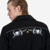 The Wilder is a black gabardine jacket with western details. It features white and metallic gold embroidery in a floral and star pattern.